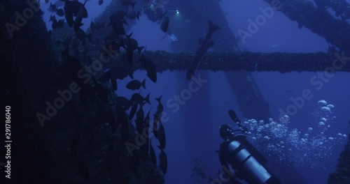 Scuba divers swim through shipwreck, slow motion