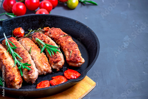 Grilled sausage and cherry tomatoes on plate over black stone background. Top view, flat lay.