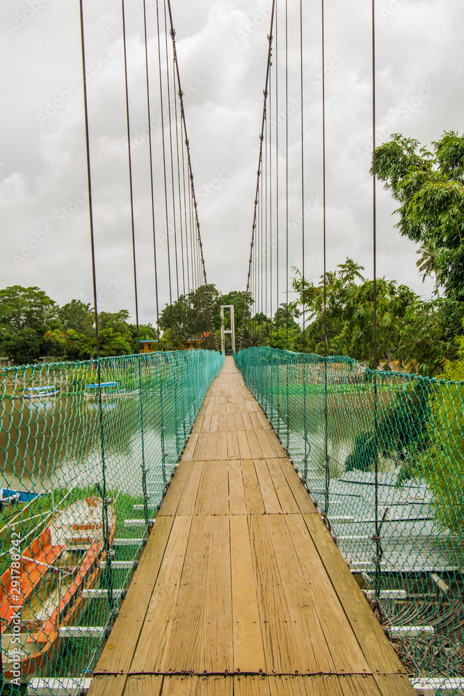 Obraz premium hanging wood floor bridge across the river with a cloudy sky