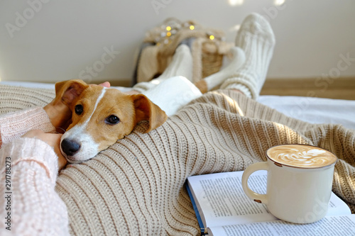 Obraz na płótnie Young woman and her adorable jack russell terrier puppy sitting on couch cozied up, covered with blanket