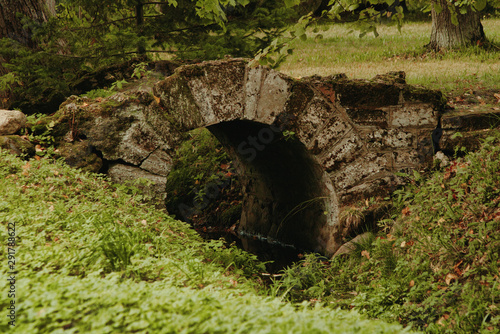 A small humpbacked stone bridge over a stream in a Oranienbaum park in Lomonosov town in Russia. Natural background with foliage in autumn close up plan. photo