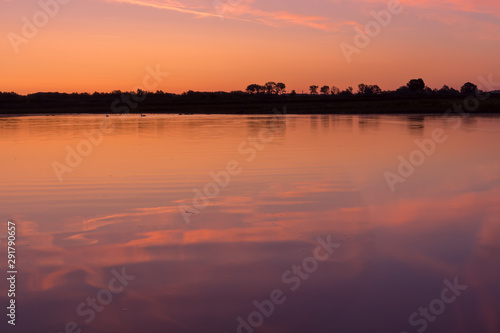 Sunrise at the border of the Netherlands and Belgium. Two countries split by the river Meuse. Picture taken from the belgium side during golden hour with reflection in the water