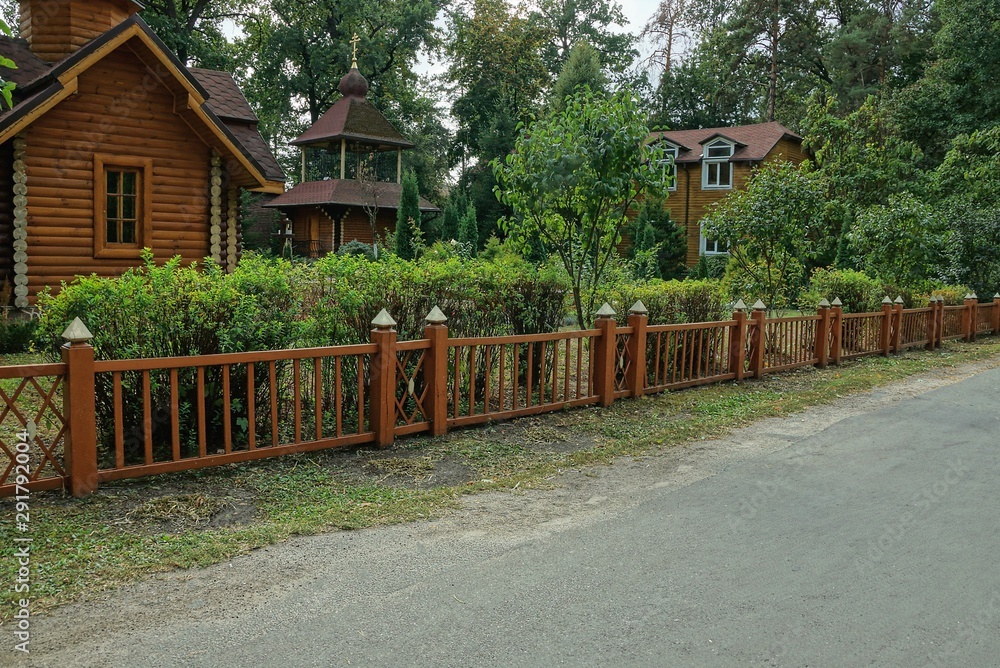 long brown decorative wooden fence in front of green vegetation by an asphalt road long brown decorative wooden fence in front of green vegetation by an asphalt road