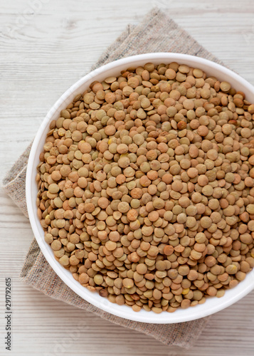 Organic green lentils in a white bowl on a white wooden background, top view. Close-up.