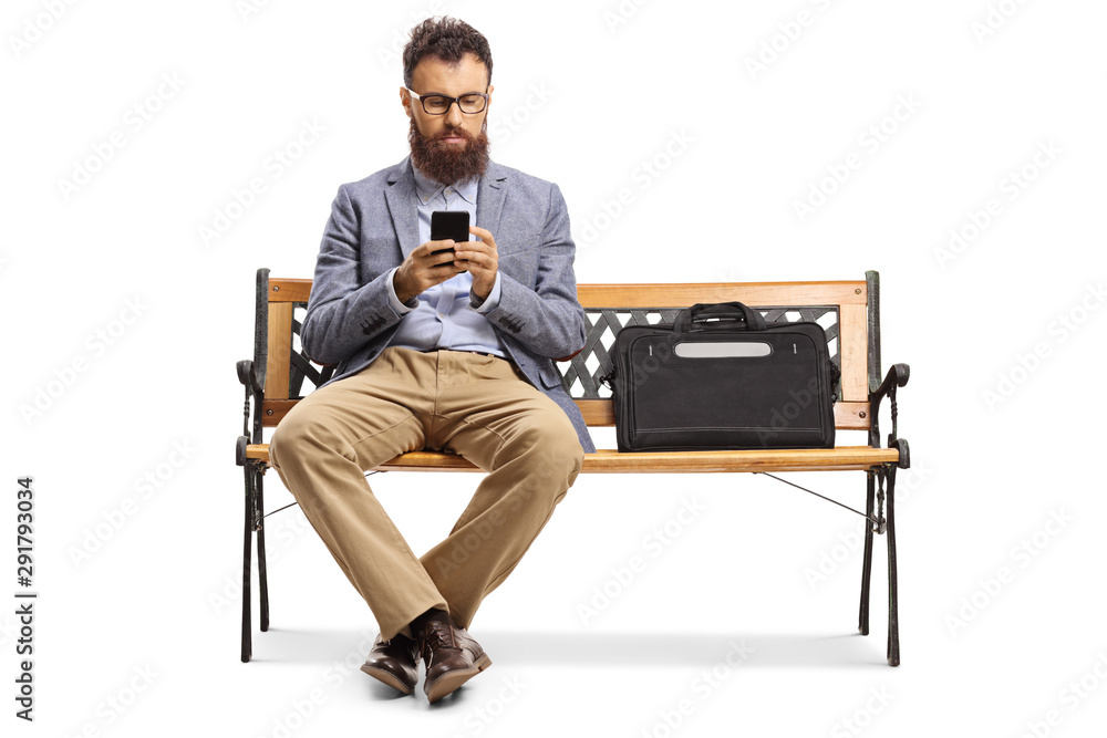 Bearded man typing on a mobile phone and sitting on a bench