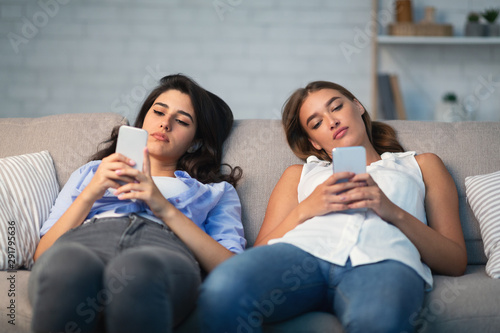 Two Girls Using Smartphones Sitting On Couch Indoor