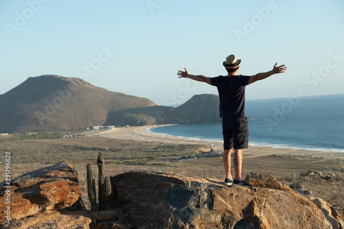 man standing with open arms in front a beach view close to a hill