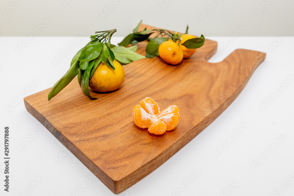 Fresh juicy clementine mandarins, winter time fruits.Half-peeled mandarin and peel on a wooden surface, minimalistic still life. Mandarine or tangerine with leaves on wooden board