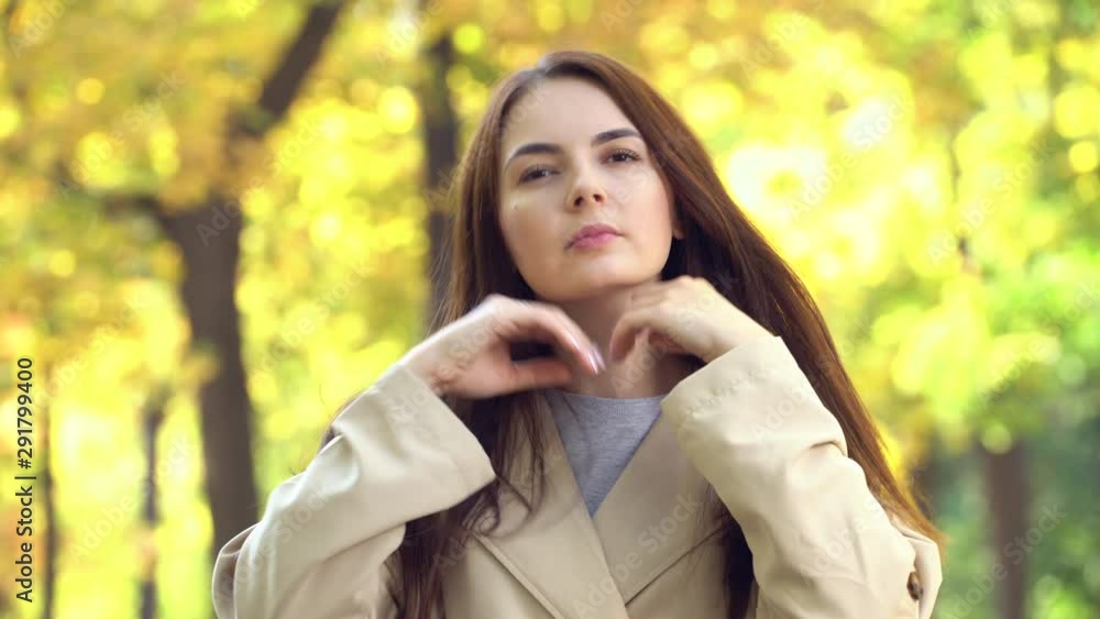 Portrait of an attractive young girl in coat or trench straightens her hair with hand Portrait of an attractive young girl in coat or trench straightens her hair with hand