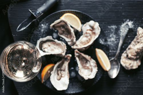 Open oysters with lemon and wine in a black plate, top view