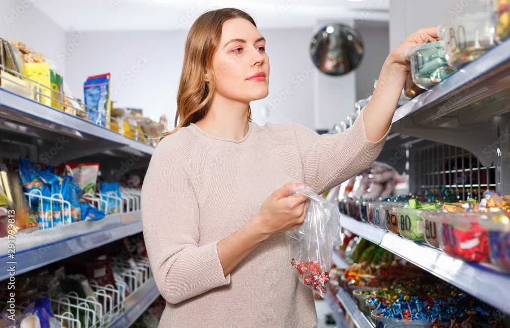 Positive woman buyer picking  different candies in cellophane bag  in store