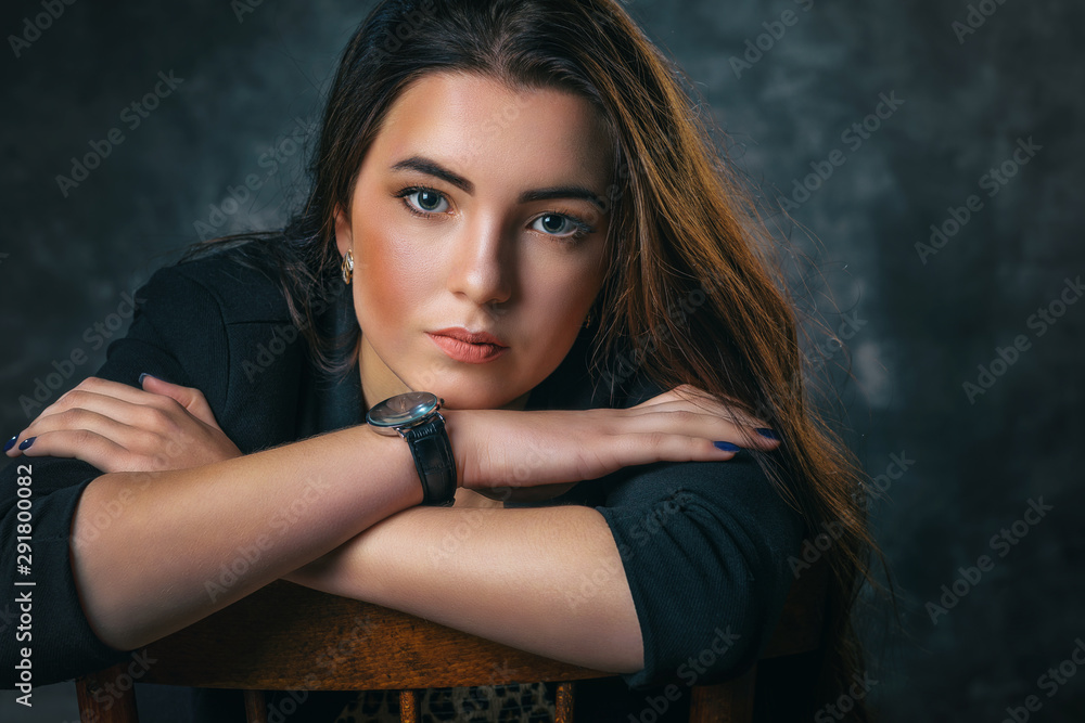 Business portrait of a beautiful brunette girl in a dark suit. Model posing on a chair, Business portrait of a beautiful brunette girl in a dark suit. Model posing on a chair,