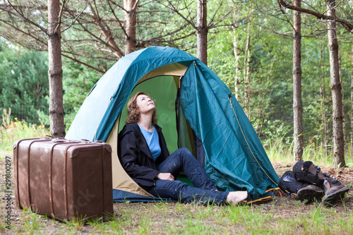 One woman enjoying inside camping tent in summer at nature forest, big cuitcase standing outside