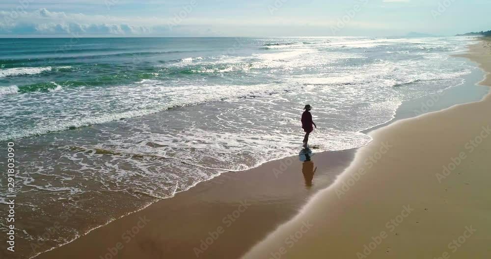 Drone y hermosa mujer con pamela paseando en soledadpor amplia playa de arena dorada 