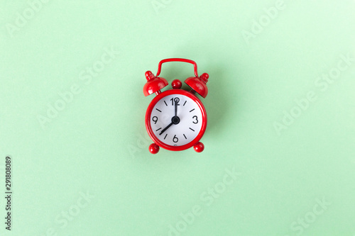 Red small alarm clock on pastel green background with copy space, top view. Minimal retro style. Time management concept. Horizontal