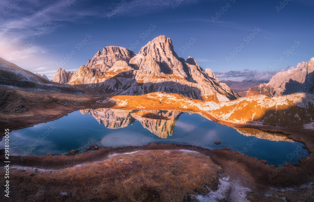 Aerial view of mountain lake with reflection at sunset in autumn. Landscape with purple sky, mountains, hills with grass, blue water in fall. Top view of high rocks. Beautiful nature. Dolomites, Italy