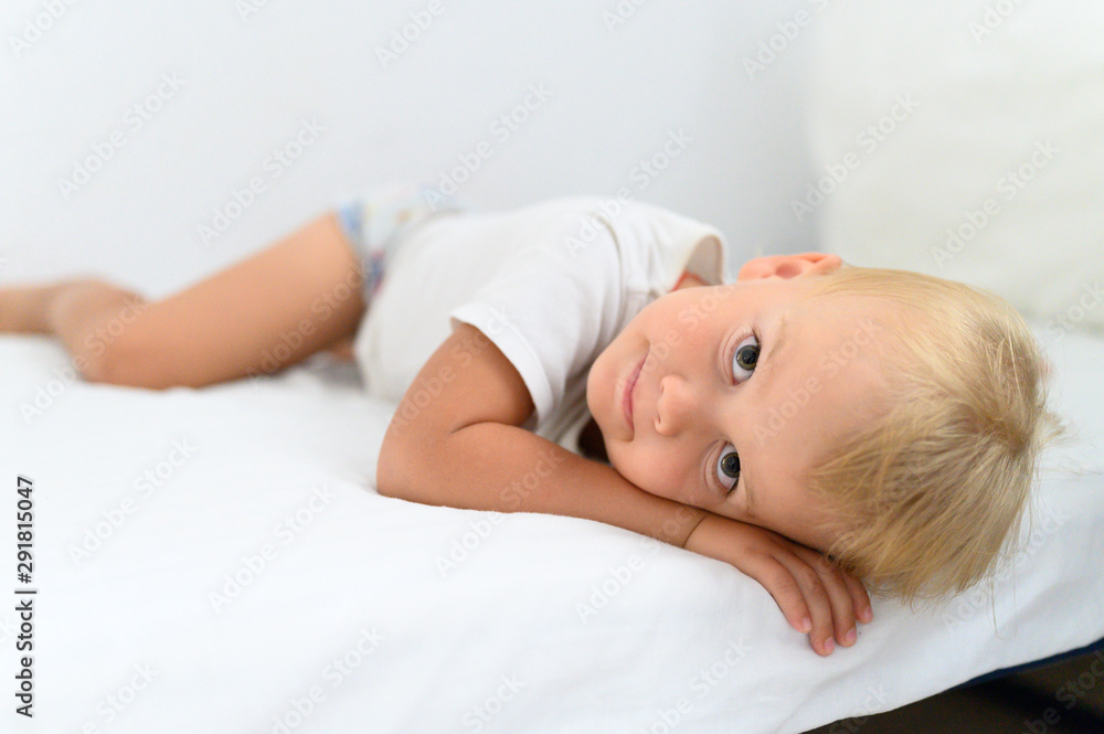 cute little smiling boy is lying on white bed cute little smiling boy is lying on white bed