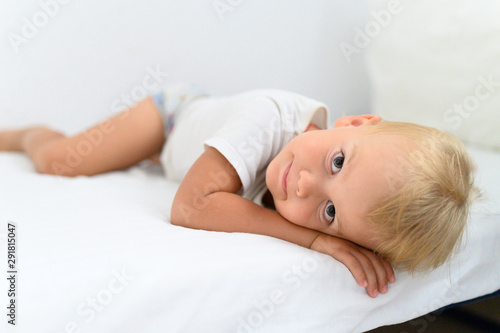 cute little smiling boy is lying on white bed