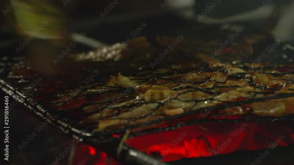 Bacon compressed between metal wires, grilling over glowing red charcoal, as a cook uses a brush to flavor it Bacon compressed between metal wires, grilling over glowing red charcoal, as a cook uses a brush to flavor it