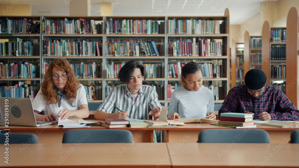 Portrait of busy youth students studying in library reading books writing notes sitting at desk together. Academic education, lifestyle and people concept. Portrait of busy youth students studying in library reading books writing notes sitting at desk together. Academic education, lifestyle and people concept.