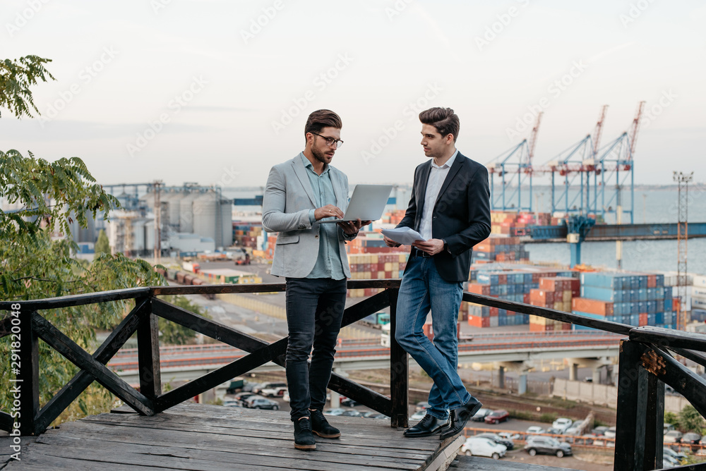 Two business partners discussing the meeting with laptop and contract, outdoor on background of the seaport