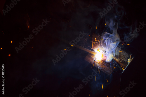 Arc welding. Welding of two sheets of metal by electrode in inert gases. Type MMA. A bright flash of light and a sheaf of sparks in a cloud of smoke. Miniature Universe. Free space for inscriptions. © INTHEBLVCK
