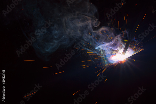 Arc welding. Welding of two sheets of metal by electrode in inert gases. Type MMA. A bright flash of light and a sheaf of sparks in a cloud of smoke. Miniature Universe. Free space for inscriptions.