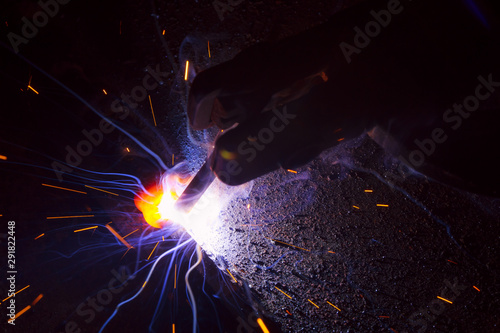 Arc welding. Welding of two sheets of metal by electrode in inert gases. Type MMA. A bright flash of light and a sheaf of sparks in a cloud of smoke. Miniature Universe. Free space for inscriptions.