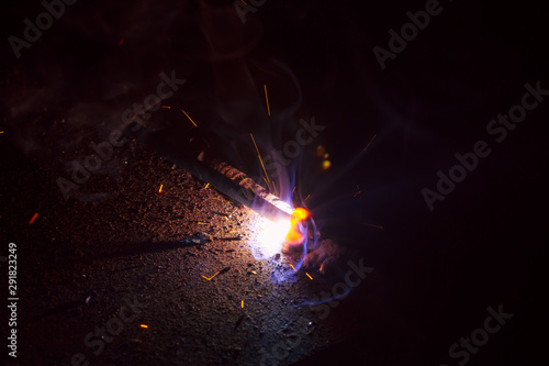 Arc welding. Welding of two sheets of metal by electrode in inert gases. Type MMA. A bright flash of light and a sheaf of sparks in a cloud of smoke. Miniature Universe. Free space for inscriptions.