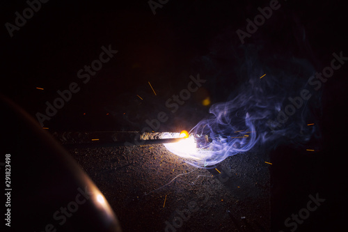 Arc welding. Welding of two sheets of metal by electrode in inert gases. Type MMA. A bright flash of light and a sheaf of sparks in a cloud of smoke. Miniature Universe. Free space for inscriptions.