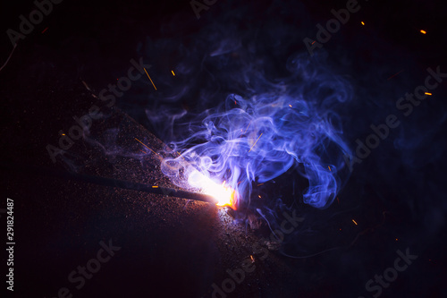 Arc welding. Welding of two sheets of metal by electrode in inert gases. Type MMA. A bright flash of light and a sheaf of sparks in a cloud of smoke. Miniature Universe. Free space for inscriptions.