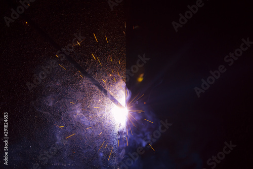 Fototapeta Naklejka Na Ścianę i Meble -  Arc welding. Welding of two sheets of metal by electrode in inert gases. Type MMA. A bright flash of light and a sheaf of sparks in a cloud of smoke. Miniature Universe. Free space for inscriptions.