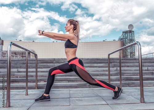 A sports girl in the city in the summer does a warm-up before training, stretching muscles, workout in the fresh air, sportswear, leggings top, sneakers. Life style motivation, active life position.