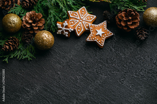 Christmas background with homemade gingerbread cookies, evergreen branches and decorations on black table. Festive food, New Year celebration traditions