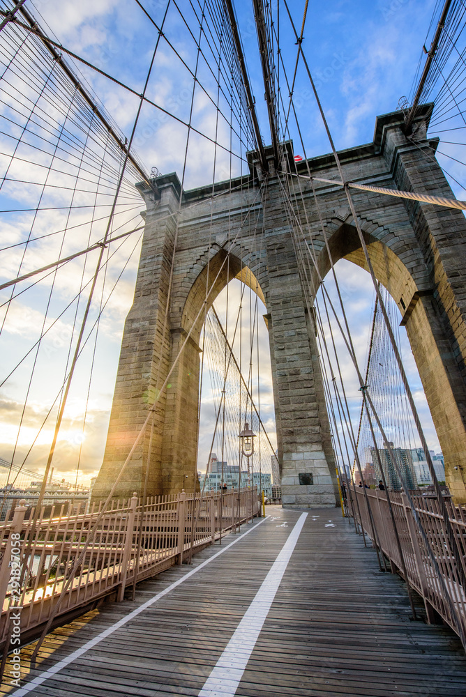 Fototapeta Sun shines through the Brooklyn Bridge with views of Manhattan during Sunrise