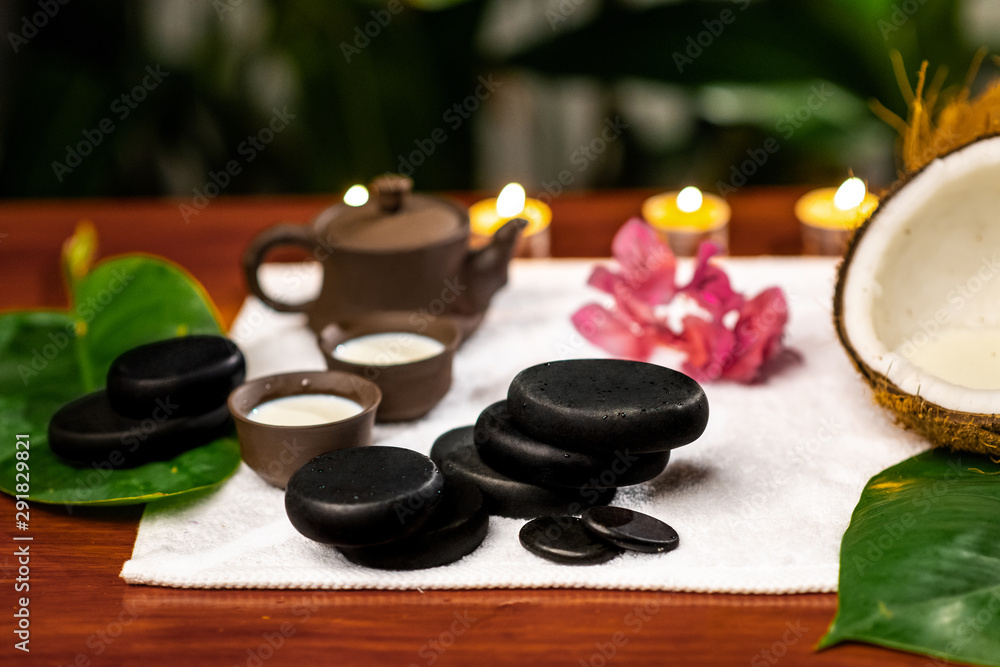 A terry towel on which there is a clay teapot and cups for drinks with milk, stones for stone therapy, lighted candles, a mangolia flower and a twisted terry towel on a wooden table A terry towel on which there is a clay teapot and cups for drinks with milk, stones for stone therapy, lighted candles, a mangolia flower and a twisted terry towel on a wooden table