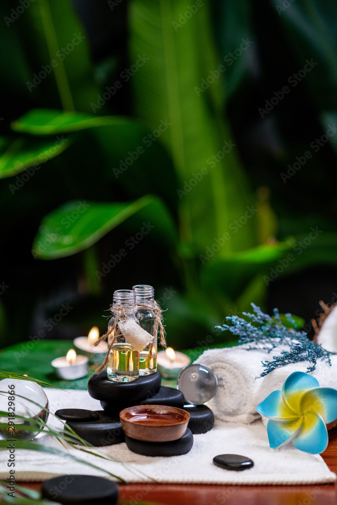 Fototapeta premium Two jars of aromatic oils standing on stones for a therapy stone and located on a terry towel next to which a flower lies, there are transparent spheres a rolled towel and a sprig of lavender