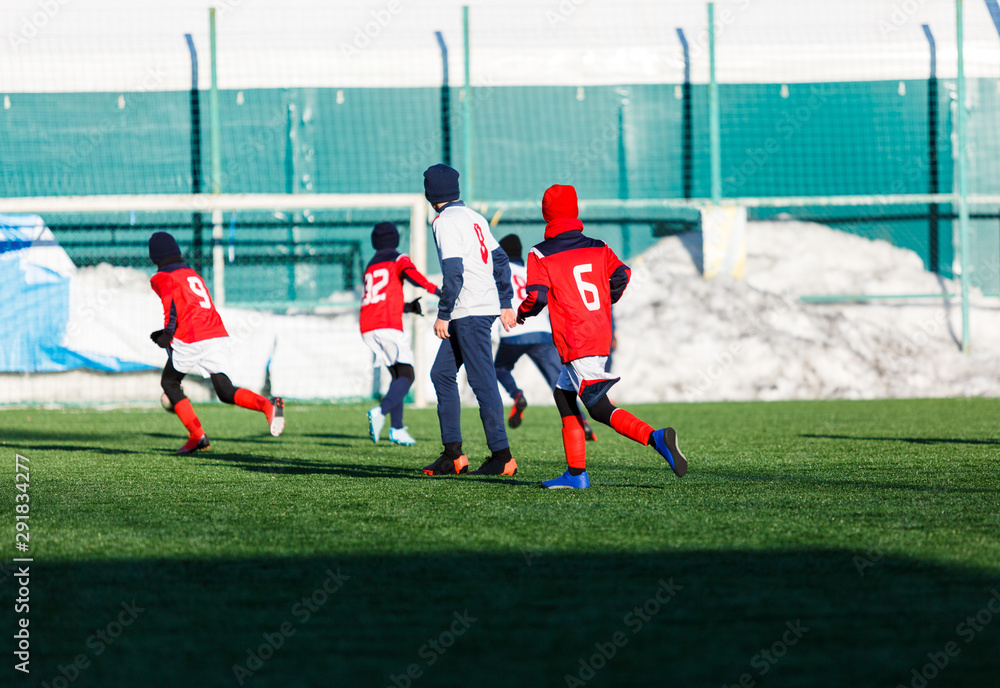 Fototapeta premium Boys in white and red sportswear plays football on field, dribbles ball. Young soccer players with ball on green grass. Training, football, active lifestyle for kids , winter sport