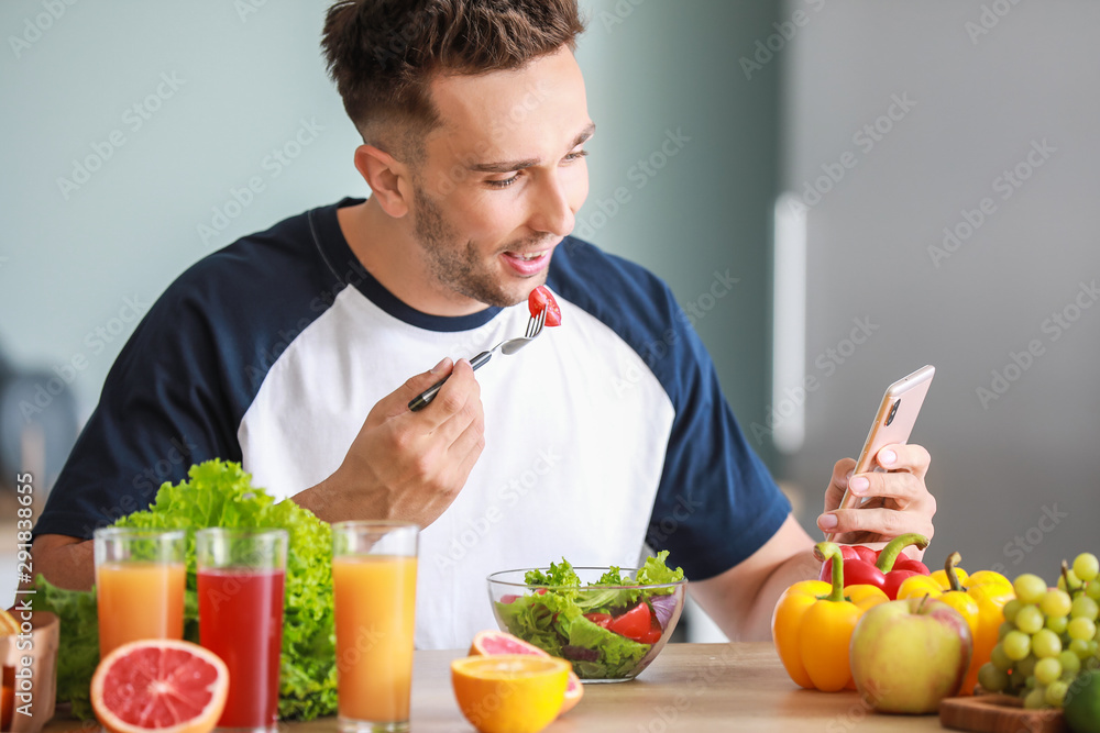 Handsome man counting calories while eating salad in kitchen. Weight loss concept Handsome man counting calories while eating salad in kitchen. Weight loss concept