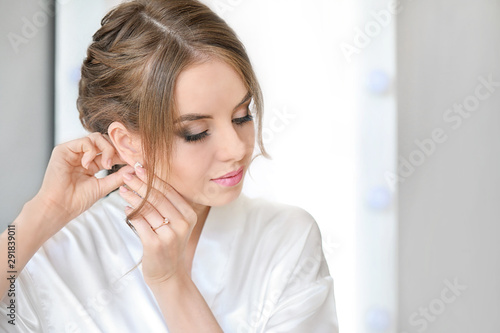 Beautiful young bride wearing earrings before wedding ceremony at home