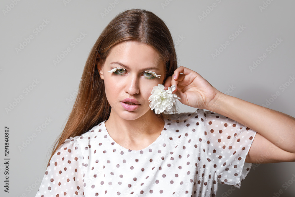 Young woman with creative eyelashes and flower on grey background