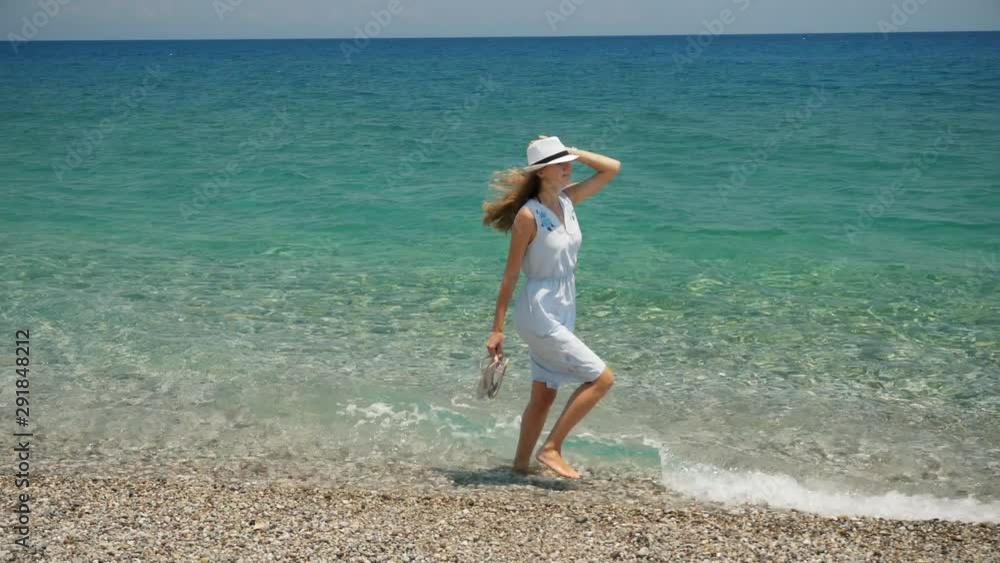 Young beautiful caucasian girl with white hat walks along the beach coastal view Young beautiful caucasian girl with white hat walks along the beach coastal view