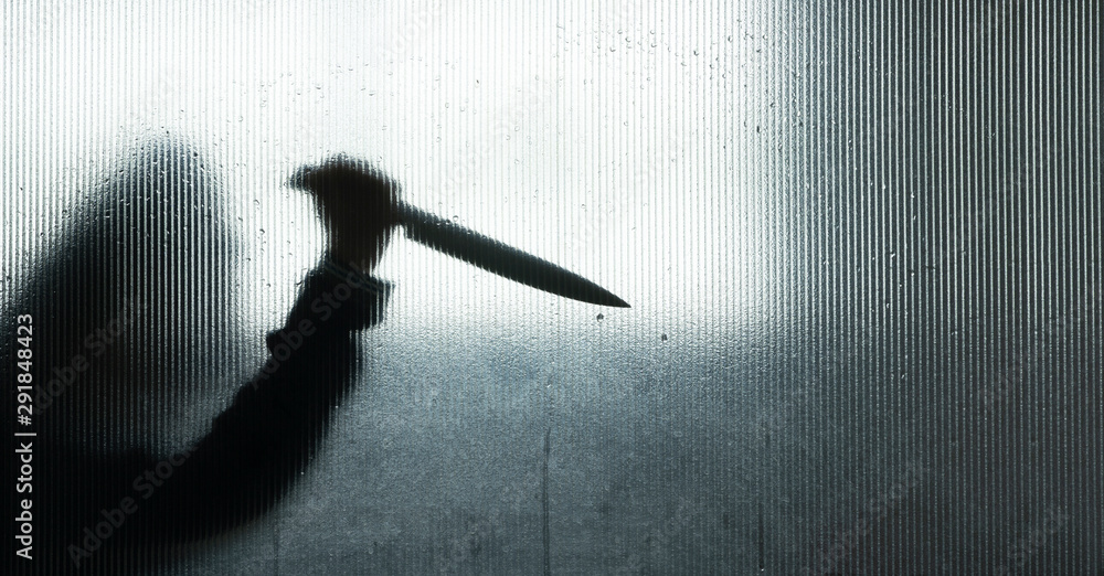 Fototapeta premium Murderer or robber with big knife in hand behind Frosted glass in the bathroom background,concept of scary crime scene of horror or thriller movies,Halloween theme,Silhouette style