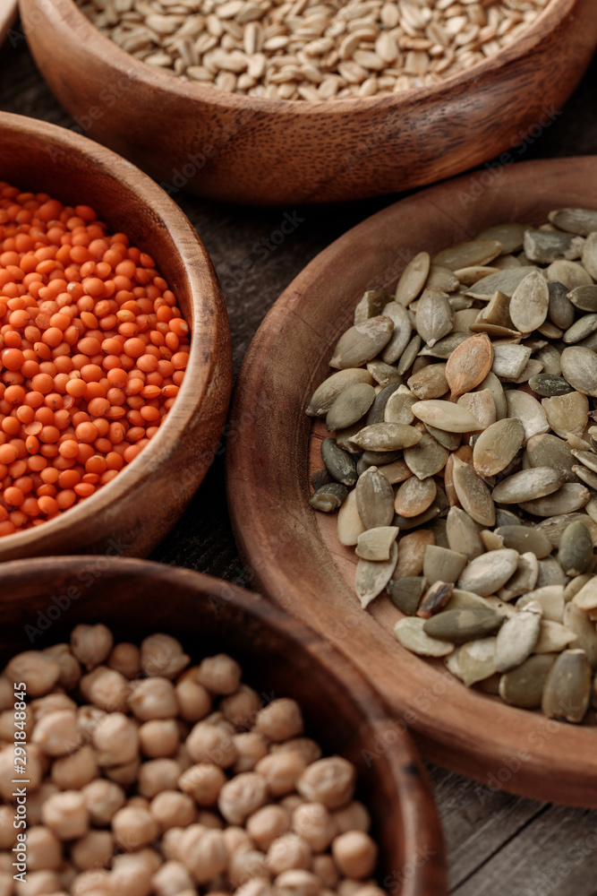 Fototapeta premium close up view of wooden bowls with chickpea, lentil, oatmeal and pumpkin seeds