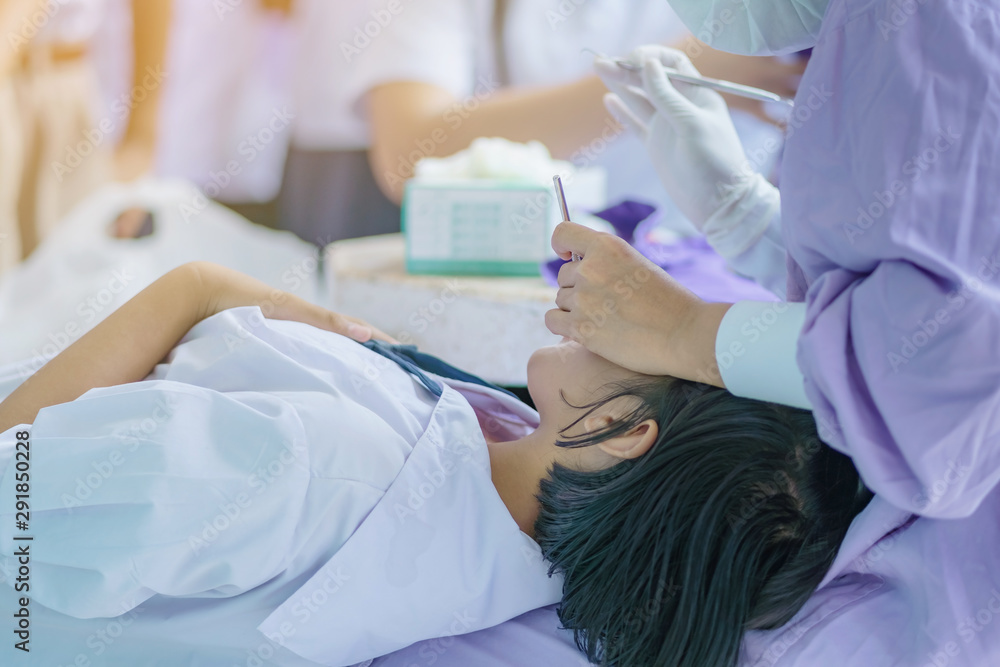 Female dentist examining teeth of a student with mouth mirror and probe checking in school. Female dentist examining teeth of a student with mouth mirror and probe checking in school.