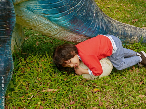 Little baby girl lying on a dinosour egg, pretending she is a dinosour mother, and hoping the egg will hatch soon © OleCNX