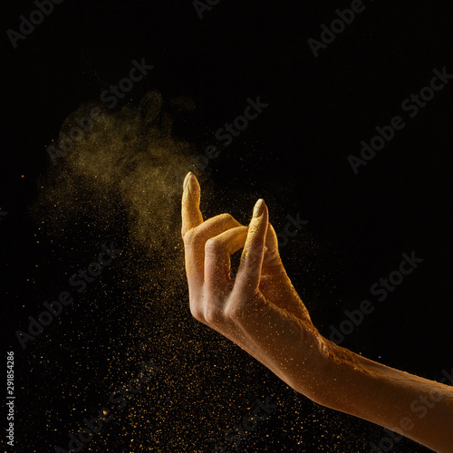 A cloud of golden powder on a black background with copy space. A woman's hand pours powder. Holi holiday concept photo