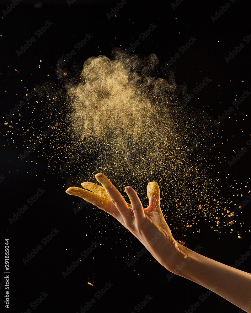 Beautiful photo of female hand throwing gold dust on a black background