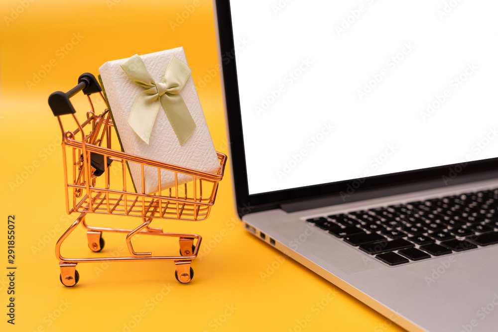 Shopping cart model, laptop and gift box on yellow background
