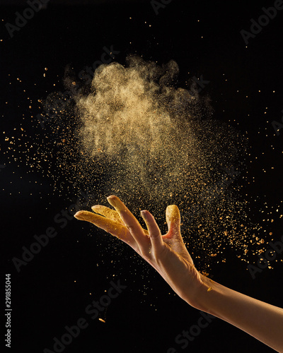 Beautiful photo of female hand throwing gold dust on a black background with copy space. Layout for your ideas. photo